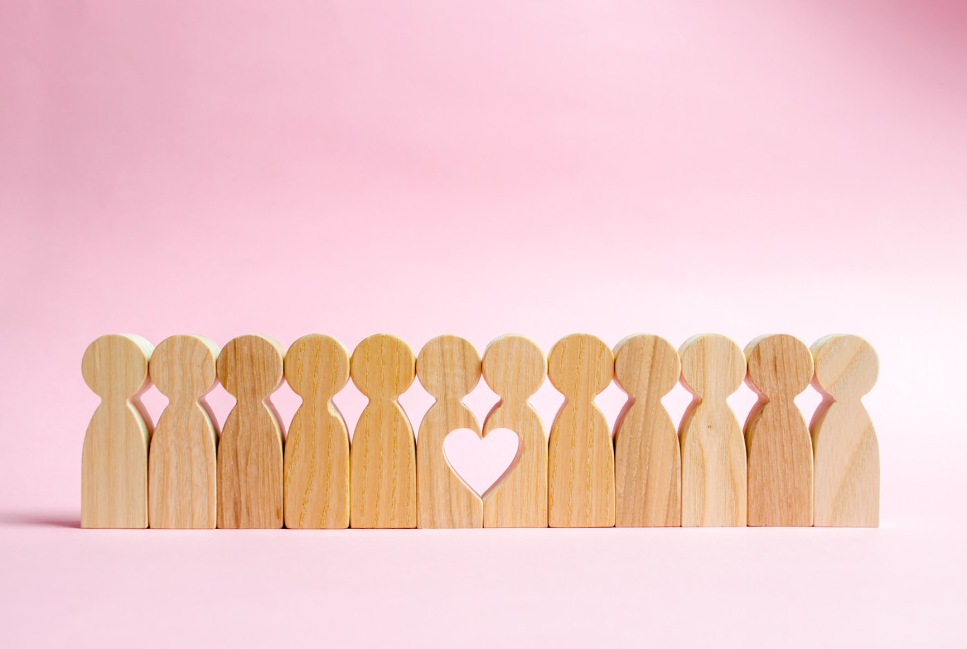 A row of wooden figures standing side-by-side, with a heart carved into the center two figures
